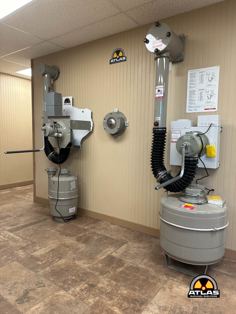 Industrial equipment room with gray generators, hoses, and a vertical exhaust pipe; Atlas Survival Shelters logo on the wall.