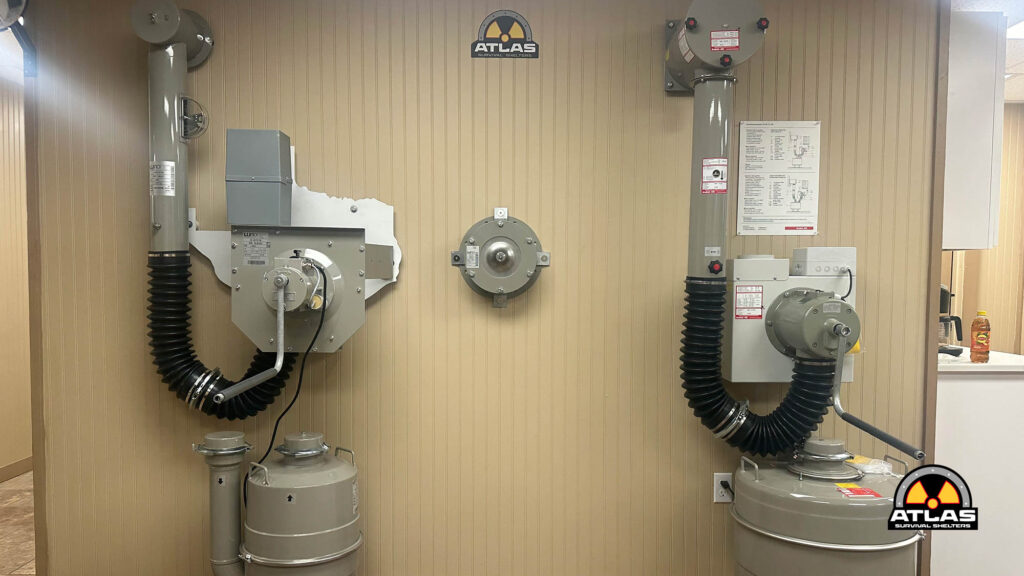 Industrial utility room with HVAC ducts, control panels, and gas cylinders; Atlas Survival Shelters logo on the wall.