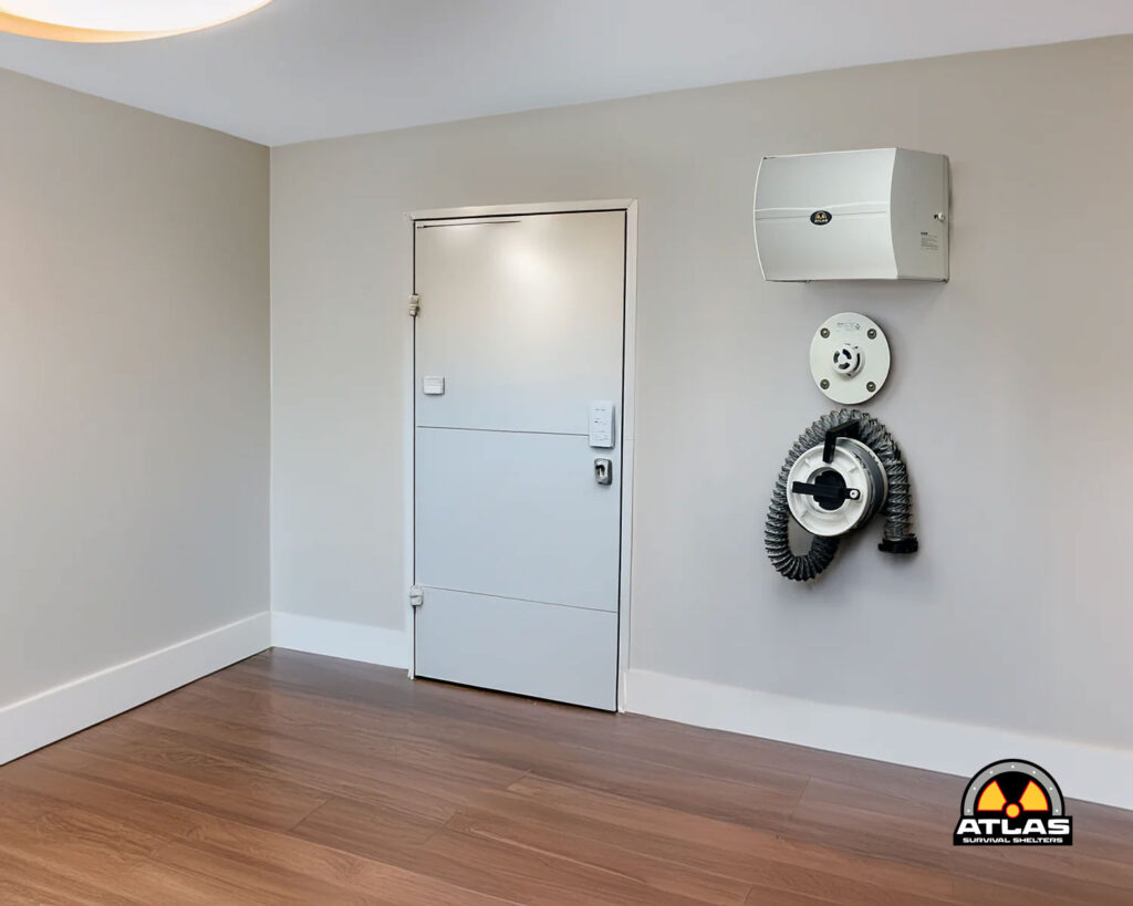 Interior with a grey metal door, wall-mounted equipment (white unit and circular hose reel) on the right; wood-look flooring.