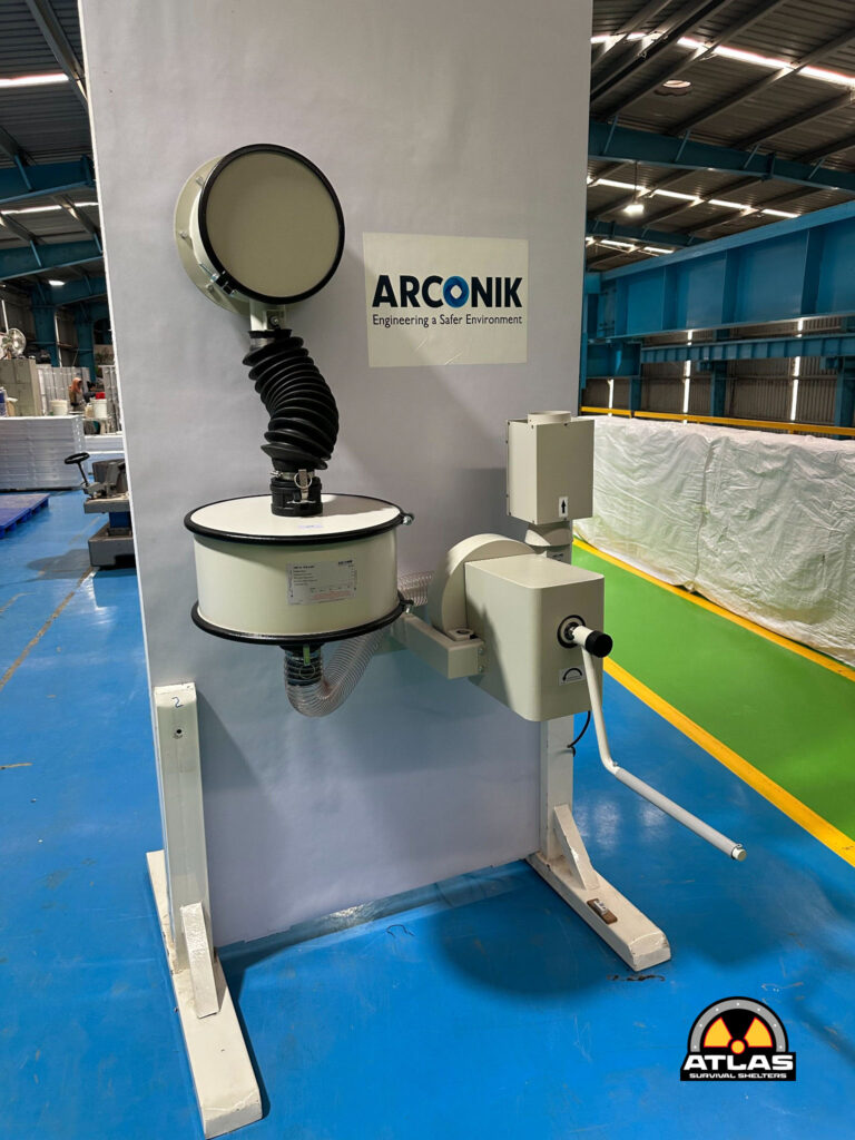 Industrial equipment setup in a factory with an Arconik sign on a gray pillar and a large circular duct connected to a white machine.