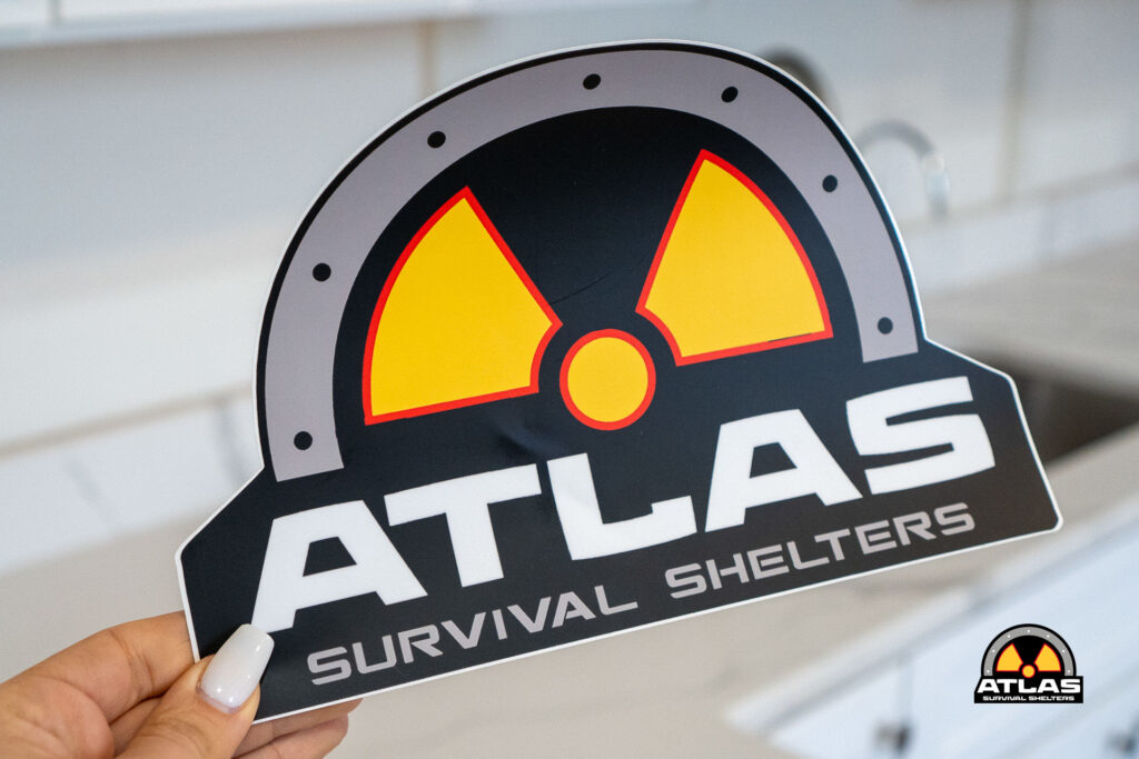 Sticker showing the ATLAS Survival Shelters logo with a yellow/red radiation symbol, held by a person.