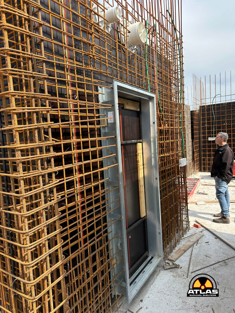 Construction site showing dense orange rebar grid around a metal-framed elevator shaft; a man stands nearby in workwear.