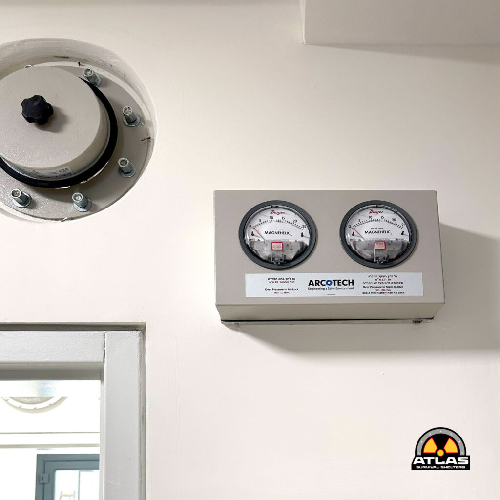 Left side shows a circular access hatch on a pale wall, with a gauge panel to the right featuring two Magnehelic meters and the ARCOTECH logo; a partial radiation warning circle is visible in the lower right corner.