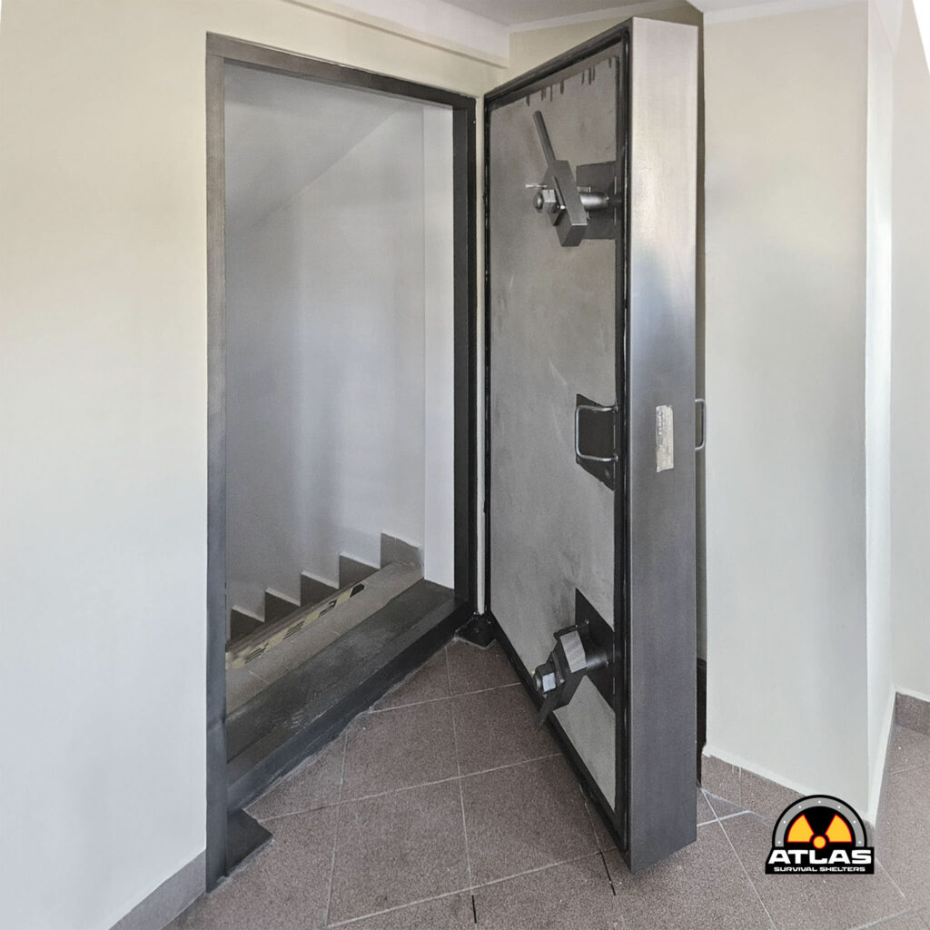 Open elevator door revealing a gray metal cabin; interior visible with a dark doorway and a logo for Atlas Survival Shelters in the bottom-right corner.