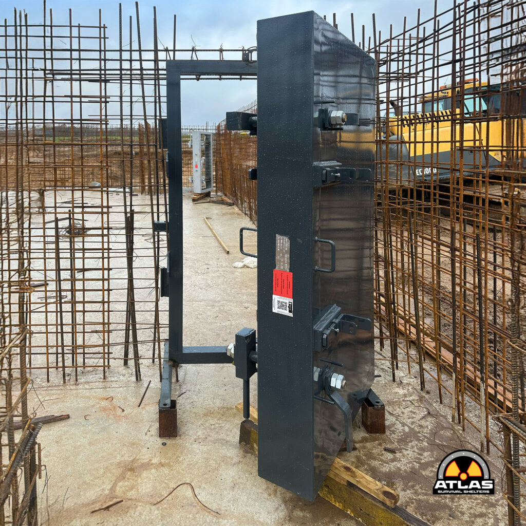 Construction site with rusted rebar cages around a black metal shelter frame and Atlas Survival Shelters logo in the bottom-right corner.