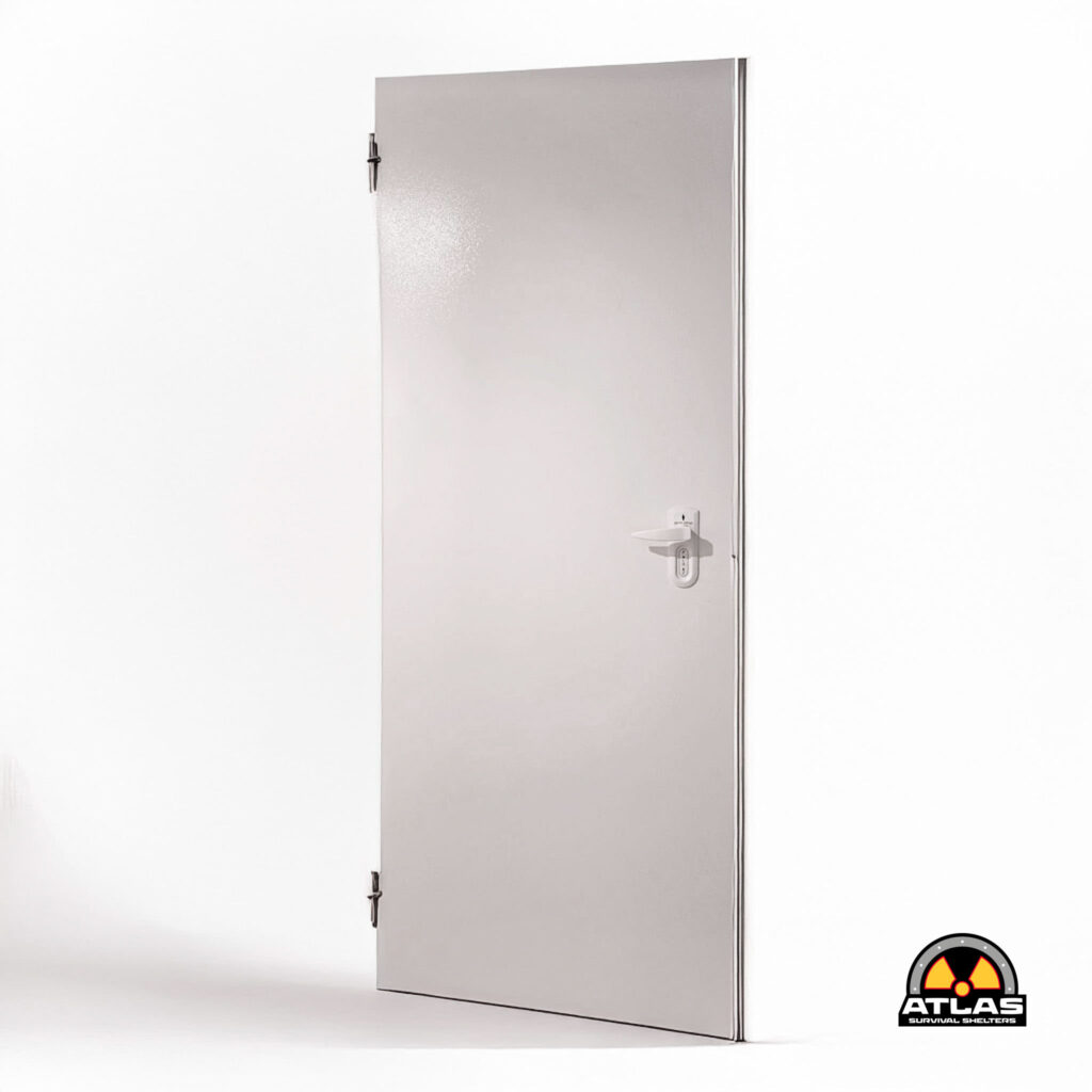 Silver metal blast door standing upright against a white wall; Atlas Survival Shelters logo visible at bottom-right corner.
