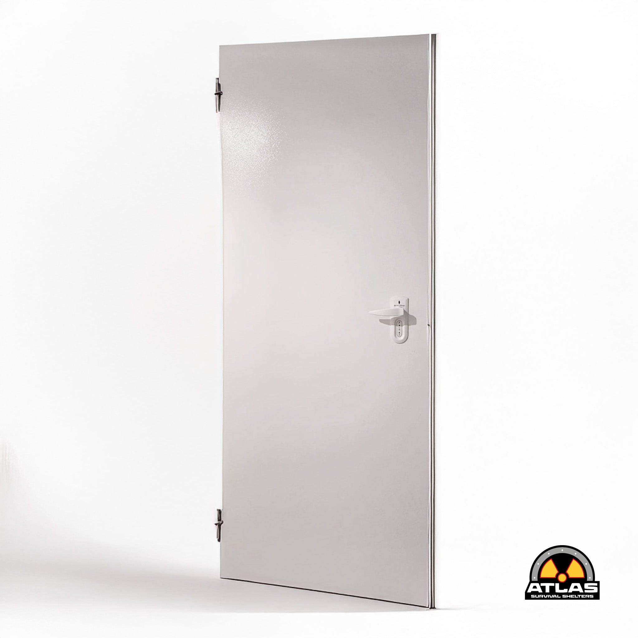 Silver metal blast door standing upright against a white wall; Atlas Survival Shelters logo visible at bottom-right corner.