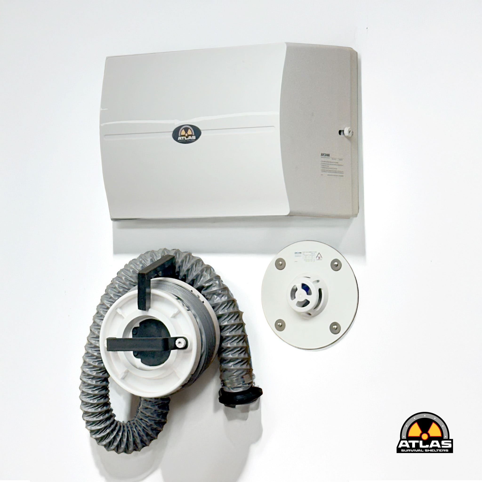 Wall-mounted white emergency shelter unit with flexible gray hose connections; Atlas Survival Shelters logo visible bottom right.