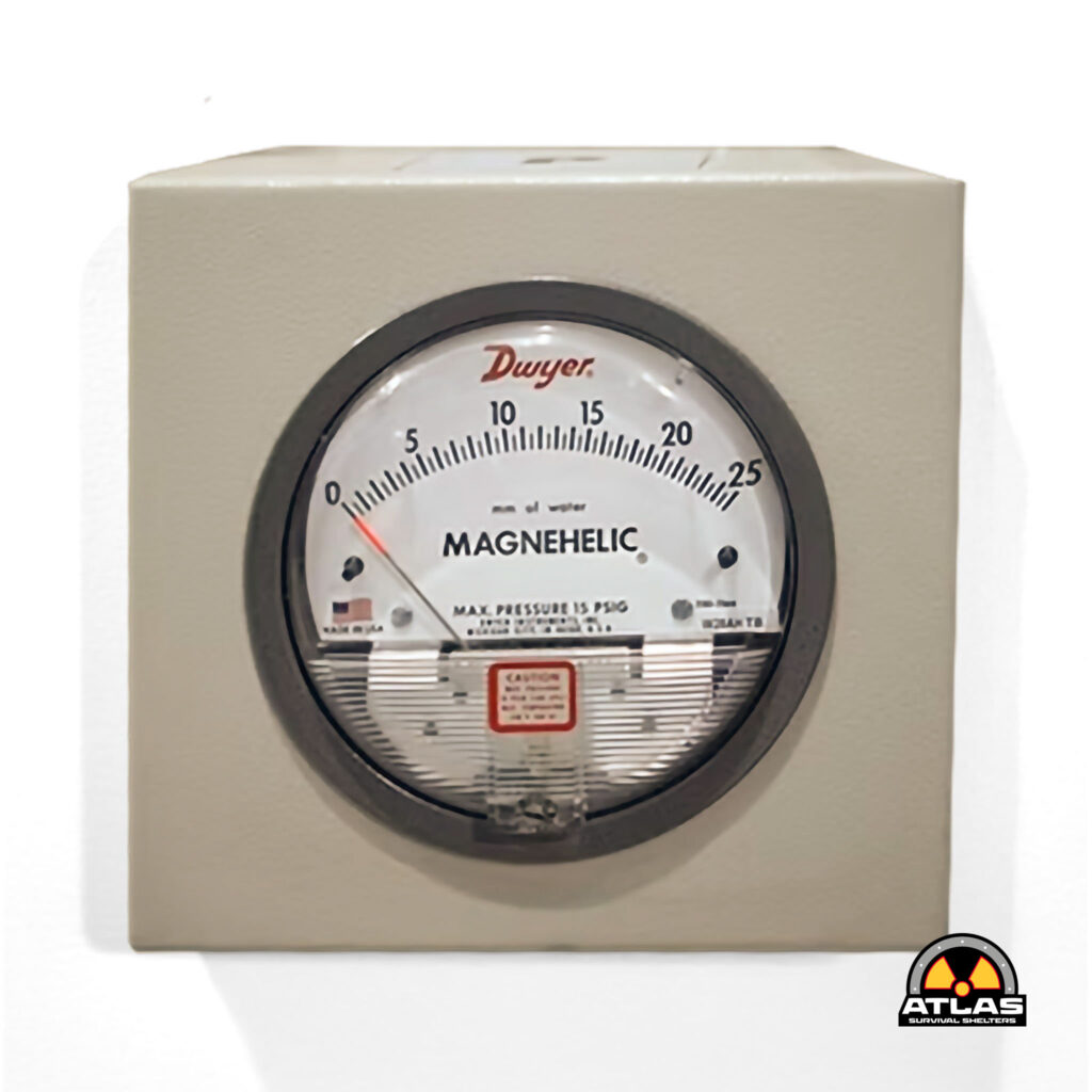 Beige metal panel with a round Magnehelic pressure gauge; Atlas Survival Shelters logo visible in the lower right corner.