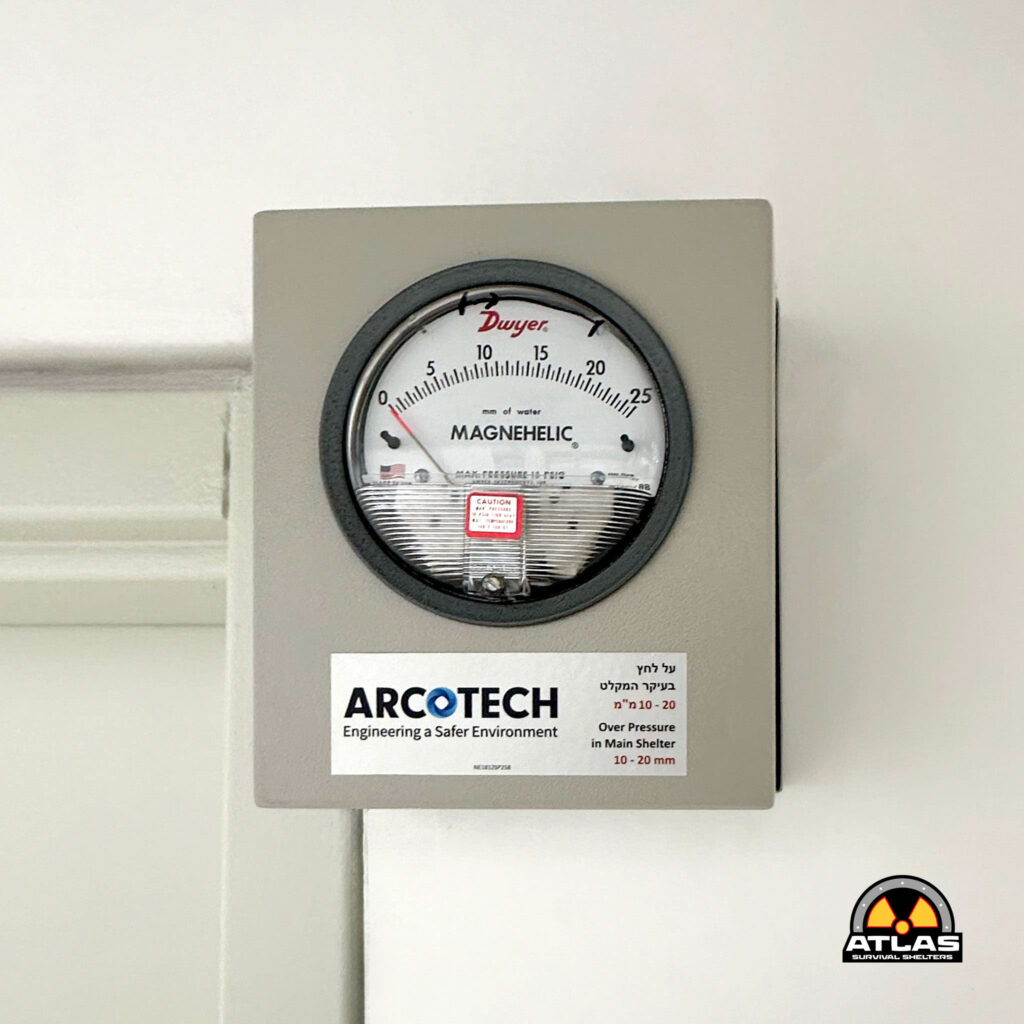 Differential pressure gauge on a gray panel, showing Magnehelic scale with ARCOTECH branding and Atlas Survival Shelters logo bottom right.