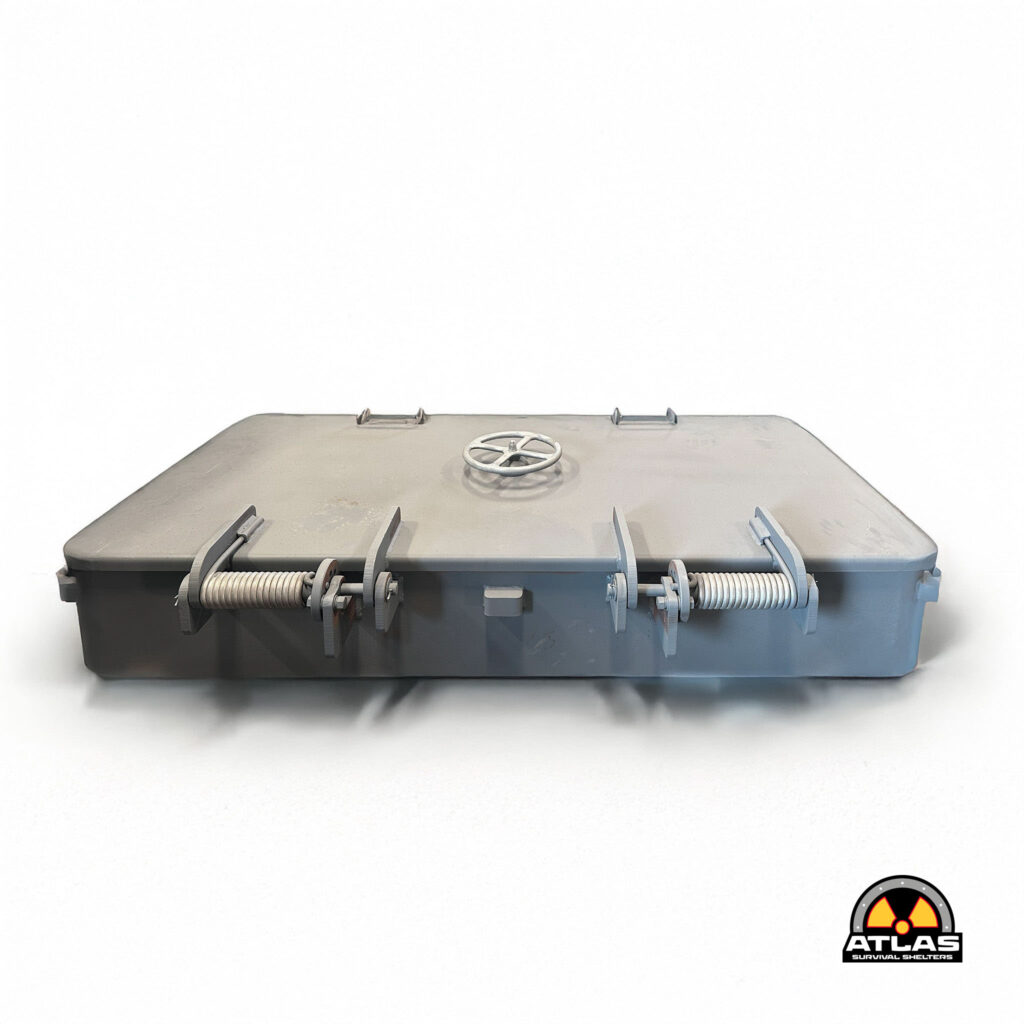 Close-up of a gray metal shelter lid with a central round wheel valve and security latches; Atlas Survival Shelters logo in the bottom-right corner.