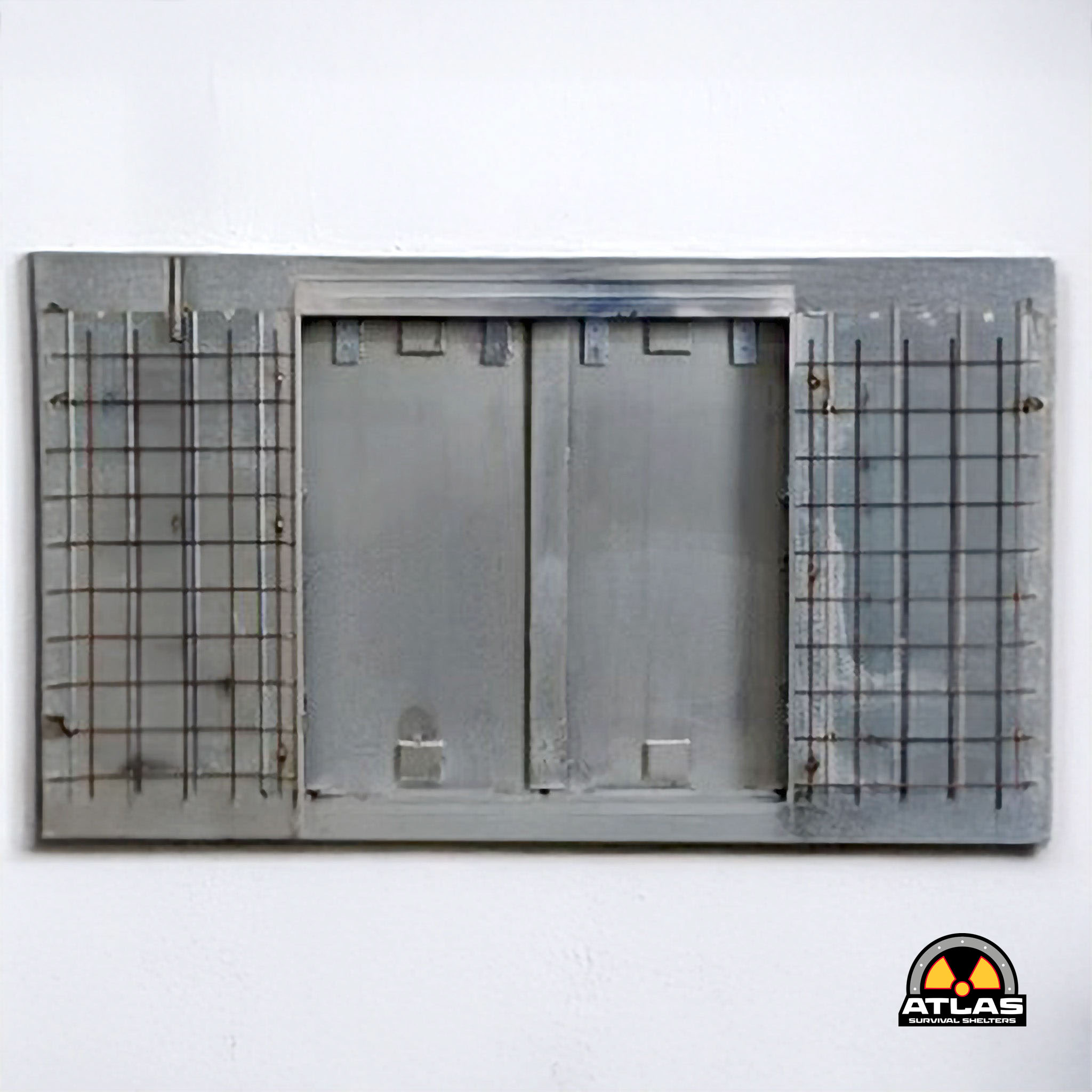 White wall with a gray metal shelter door and a partial Atlas Survival Shelters logo in the lower right corner.