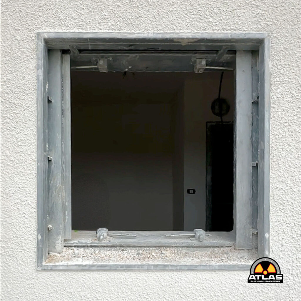 Open rectangular window frame set in a textured concrete wall, with an Atlas Survival Shelters logo visible in the bottom-right corner.